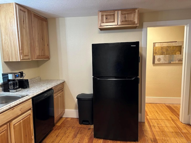 kitchen with sink, black appliances, a textured ceiling, and light wood-type flooring