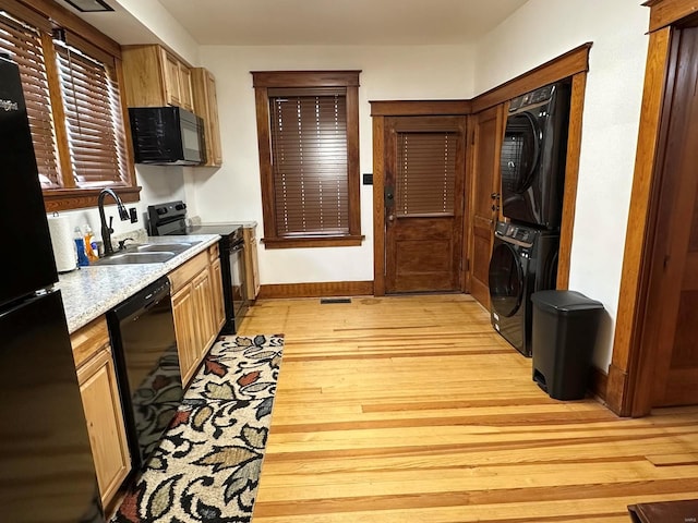 kitchen featuring sink, light wood-type flooring, stacked washing maching and dryer, and black appliances