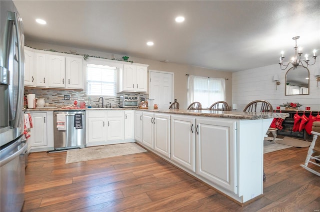 kitchen featuring white cabinets, appliances with stainless steel finishes, kitchen peninsula, and hanging light fixtures