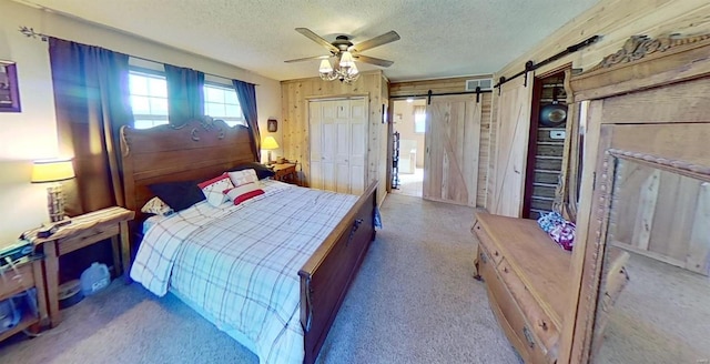 bedroom featuring a textured ceiling, a barn door, ceiling fan, and wood walls