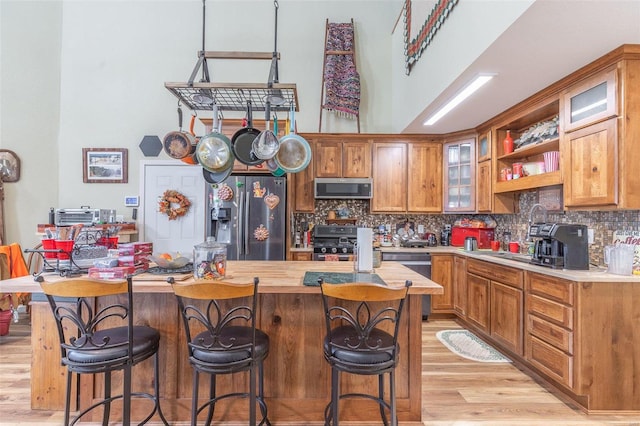 kitchen with light wood-type flooring, appliances with stainless steel finishes, tasteful backsplash, a kitchen island, and a breakfast bar area