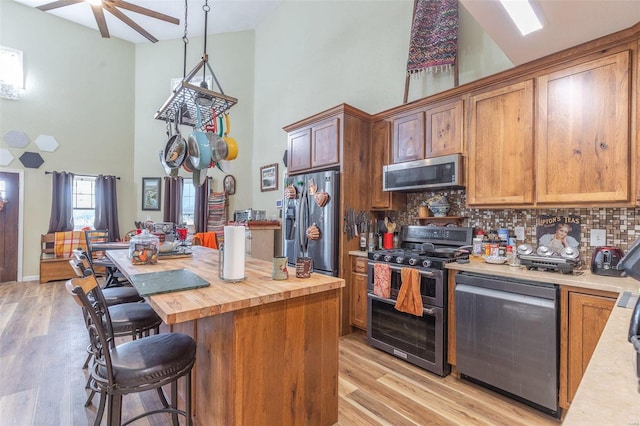 kitchen with stainless steel appliances, tasteful backsplash, wooden counters, a towering ceiling, and light wood-type flooring