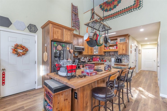 kitchen featuring decorative backsplash, appliances with stainless steel finishes, a towering ceiling, light hardwood / wood-style flooring, and butcher block countertops