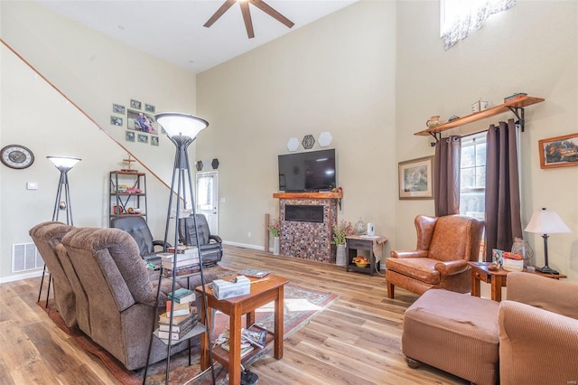 living room with ceiling fan, a high ceiling, and light hardwood / wood-style flooring