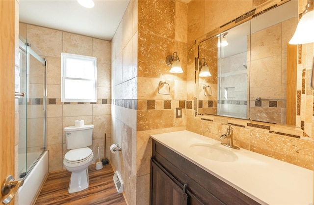 full bathroom featuring combined bath / shower with glass door, vanity, wood-type flooring, tile walls, and toilet