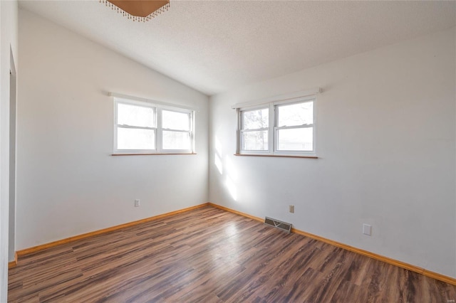 empty room with dark hardwood / wood-style floors, a textured ceiling, and vaulted ceiling