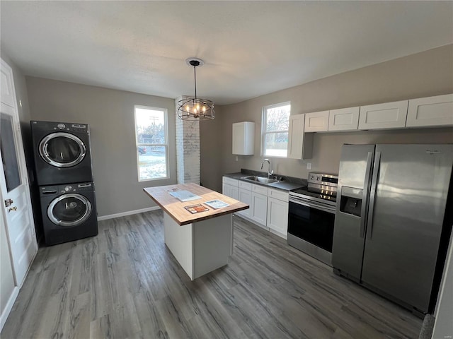 kitchen featuring stainless steel appliances, stacked washer / dryer, pendant lighting, white cabinets, and a center island