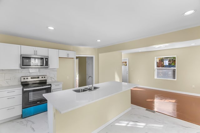 kitchen with backsplash, stainless steel appliances, sink, white cabinetry, and an island with sink