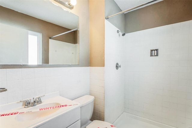 bathroom with vanity, toilet, tiled shower, and tile walls