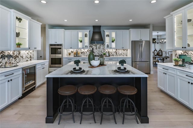 kitchen with custom exhaust hood, stainless steel appliances, beverage cooler, white cabinets, and a kitchen island