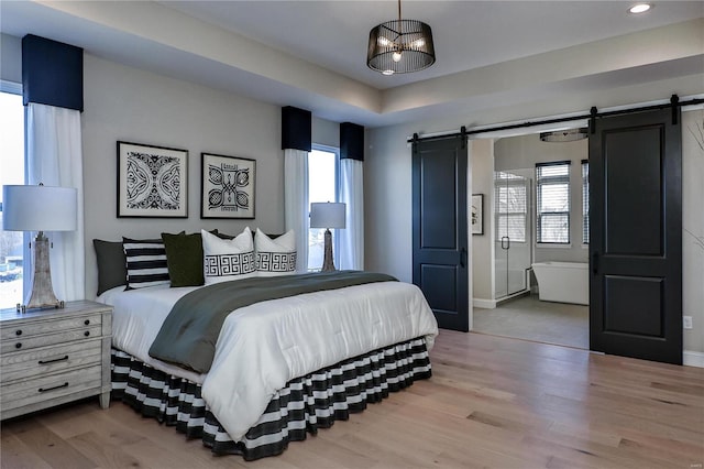 bedroom with a barn door, light wood-type flooring, and multiple windows