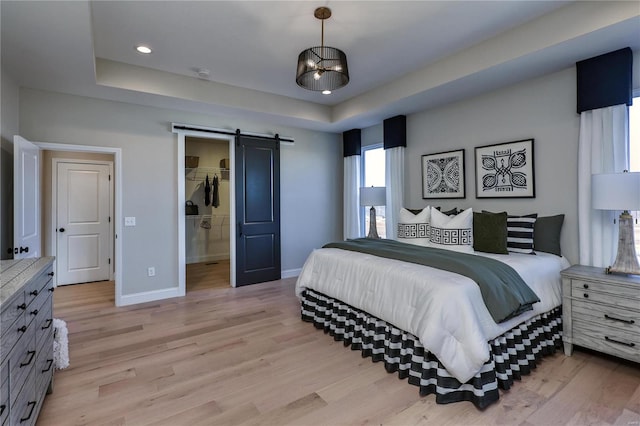 bedroom featuring a spacious closet, a barn door, light hardwood / wood-style floors, a tray ceiling, and a closet