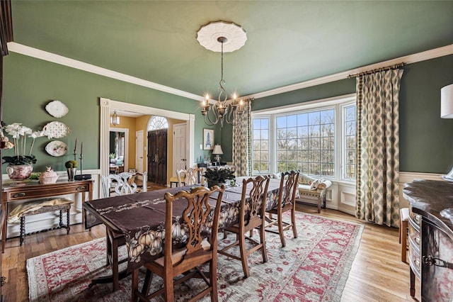 dining area with crown molding, light hardwood / wood-style floors, and an inviting chandelier