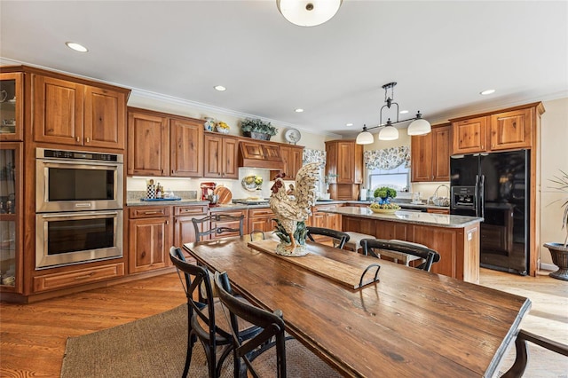 kitchen with appliances with stainless steel finishes, ornamental molding, decorative light fixtures, light hardwood / wood-style flooring, and a center island