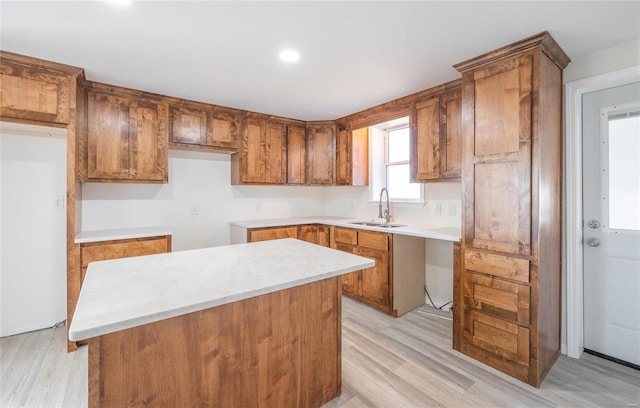 kitchen with a kitchen island, light wood-style floors, brown cabinetry, fridge, and a sink