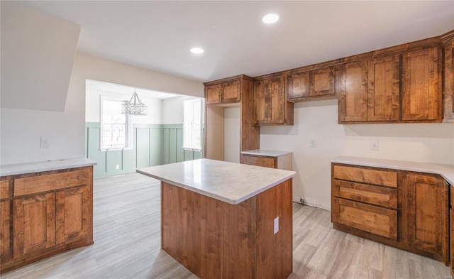 kitchen with light wood finished floors, a center island, recessed lighting, brown cabinetry, and wainscoting