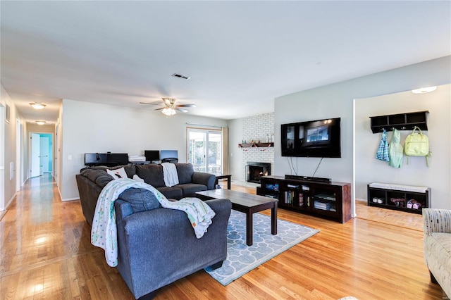 living room featuring hardwood / wood-style floors, ceiling fan, and a brick fireplace