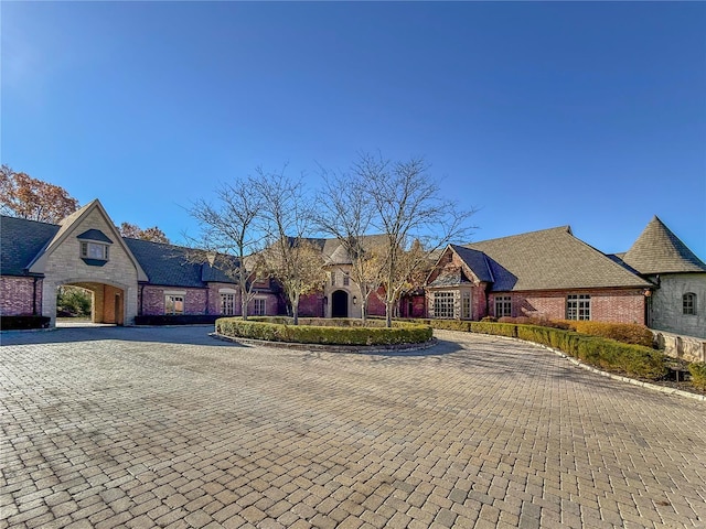 french country style house featuring stone siding, decorative driveway, and brick siding