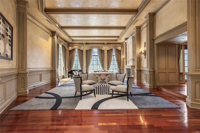 living area with decorative columns, dark wood-style floors, ornamental molding, beamed ceiling, and a decorative wall