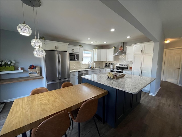 kitchen featuring stainless steel appliances, wall chimney range hood, pendant lighting, a center island, and white cabinetry