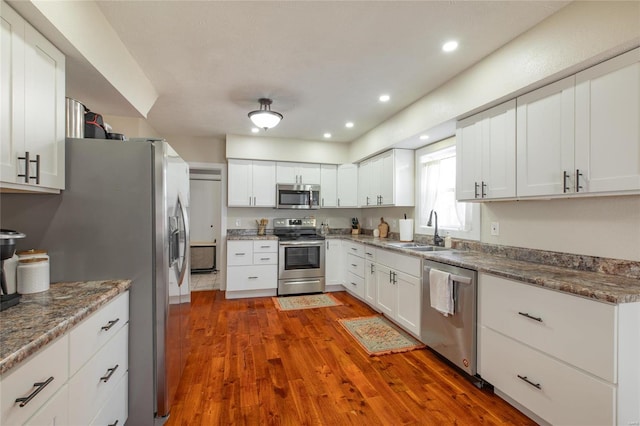 kitchen with appliances with stainless steel finishes, dark stone counters, sink, white cabinets, and dark hardwood / wood-style floors