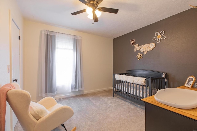 carpeted bedroom with ceiling fan and a crib