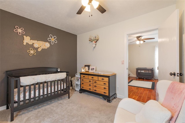 bedroom with ceiling fan, a crib, and hardwood / wood-style flooring