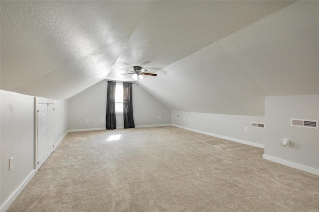 additional living space featuring a textured ceiling, ceiling fan, light colored carpet, and vaulted ceiling