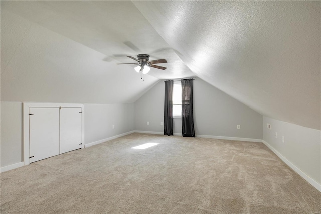 additional living space with a textured ceiling, light colored carpet, vaulted ceiling, and ceiling fan