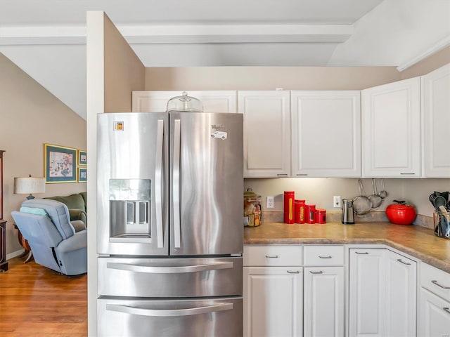 kitchen with stainless steel refrigerator with ice dispenser, light hardwood / wood-style flooring, white cabinetry, and lofted ceiling