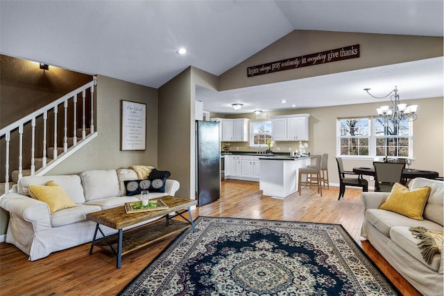 living room featuring a chandelier, vaulted ceiling, and light hardwood / wood-style flooring