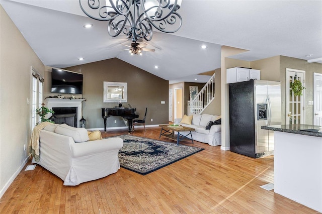 living room featuring ceiling fan with notable chandelier, vaulted ceiling, and light wood-type flooring