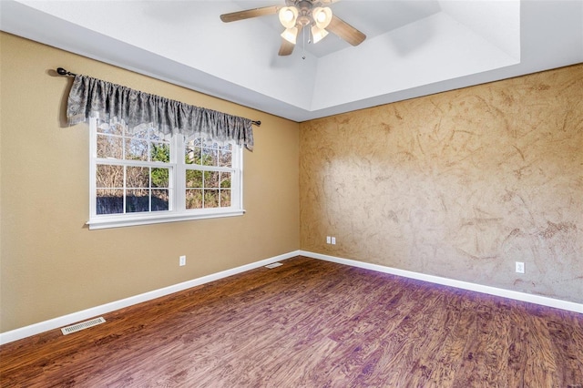 empty room featuring dark hardwood / wood-style flooring, a tray ceiling, and ceiling fan