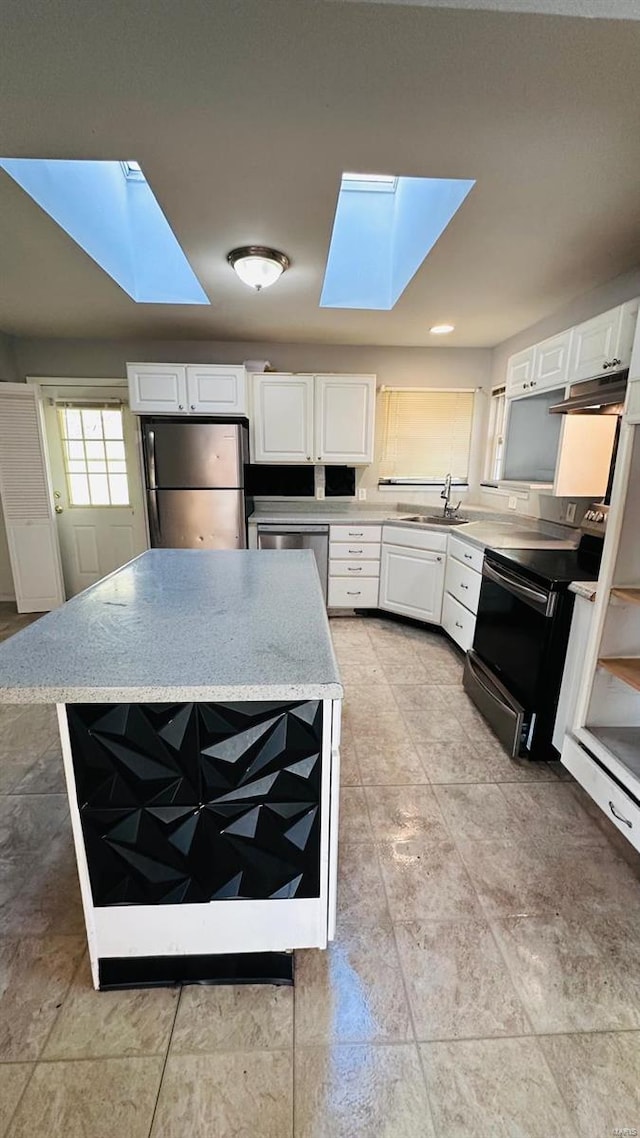 kitchen with a skylight, light stone countertops, white cabinetry, sink, and stainless steel appliances