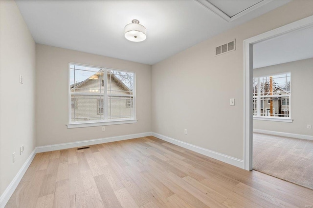 spare room with light wood-type flooring, visible vents, and baseboards