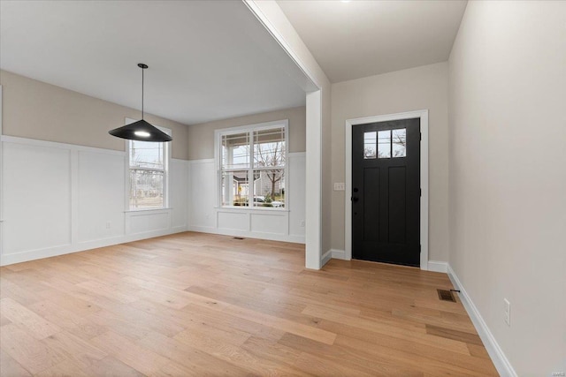 foyer entrance featuring a wainscoted wall, a decorative wall, visible vents, and light wood finished floors