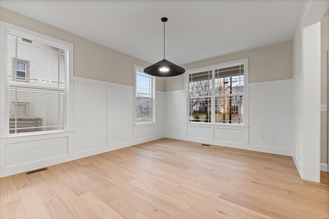 unfurnished dining area featuring a wainscoted wall, visible vents, a decorative wall, and light wood finished floors