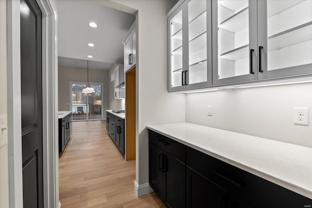 kitchen with light wood-style flooring, glass insert cabinets, light countertops, and dark cabinets