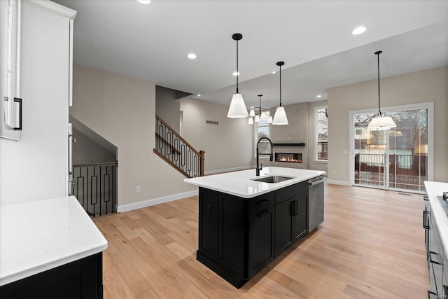 kitchen with light countertops, stainless steel dishwasher, light wood-style floors, a sink, and dark cabinetry