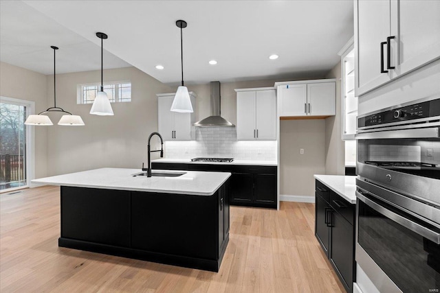 kitchen with appliances with stainless steel finishes, dark cabinets, light countertops, wall chimney range hood, and a sink