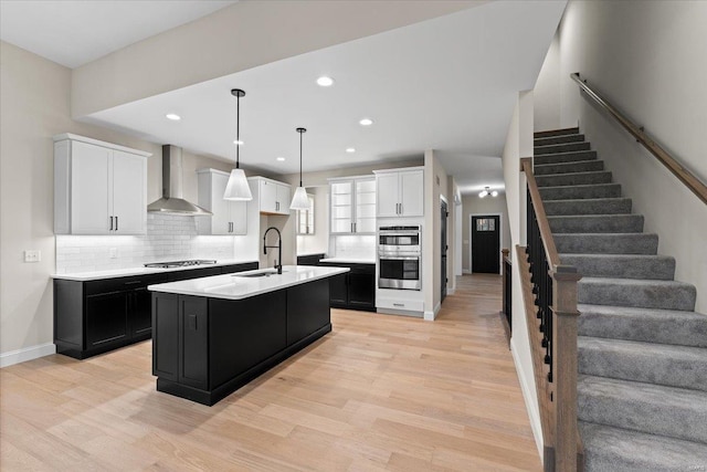 kitchen featuring tasteful backsplash, appliances with stainless steel finishes, light countertops, dark cabinetry, and wall chimney range hood