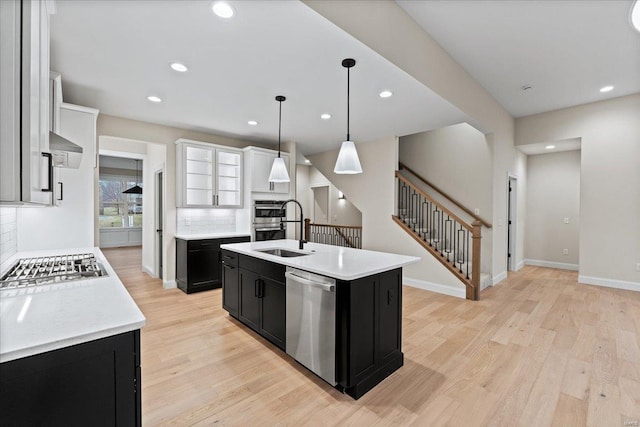 kitchen featuring appliances with stainless steel finishes, light wood-style floors, a sink, and dark cabinets