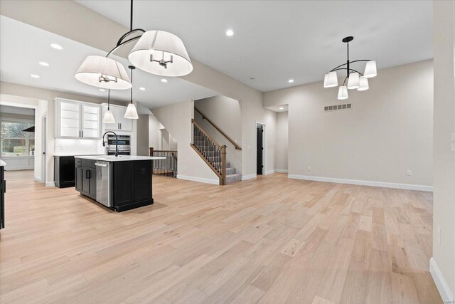 kitchen featuring visible vents, light countertops, stainless steel dishwasher, dark cabinetry, and an island with sink