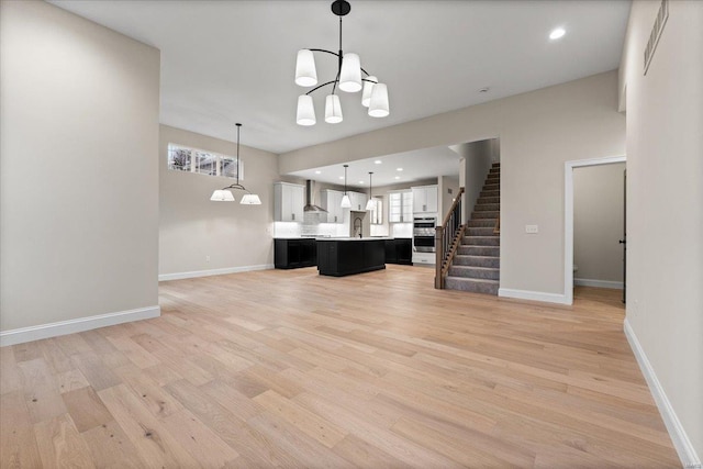 unfurnished living room with baseboards, stairway, light wood-style floors, a chandelier, and a sink