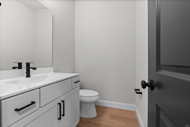 bathroom with toilet, wood finished floors, vanity, and baseboards