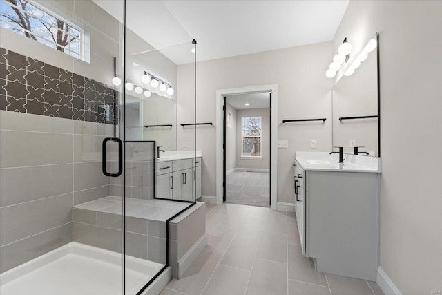 full bath with a stall shower, two vanities, a sink, and baseboards