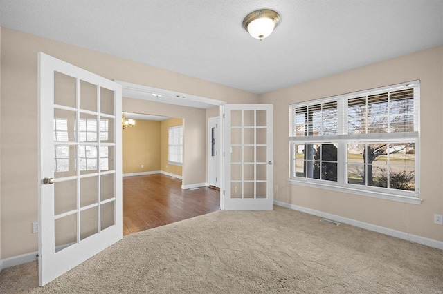 carpeted spare room with french doors, plenty of natural light, and a notable chandelier