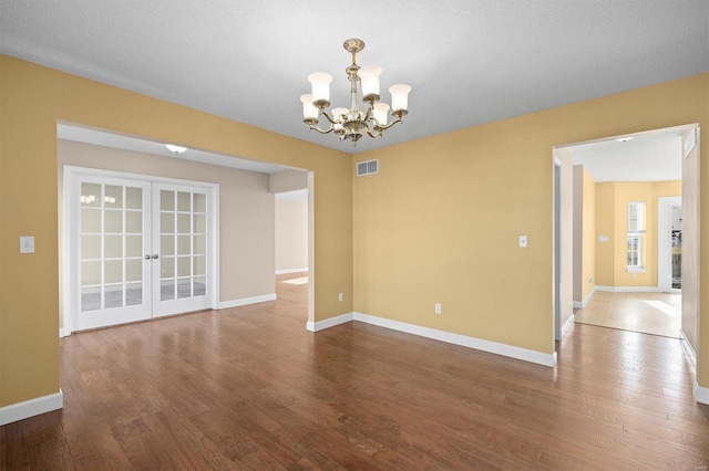 empty room with hardwood / wood-style flooring, an inviting chandelier, and french doors