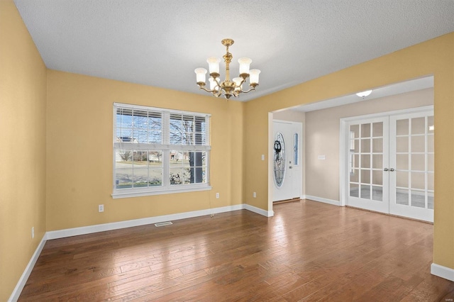 unfurnished dining area featuring french doors, hardwood / wood-style floors, a textured ceiling, and a notable chandelier