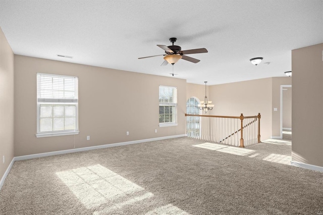 carpeted spare room featuring ceiling fan with notable chandelier and a textured ceiling